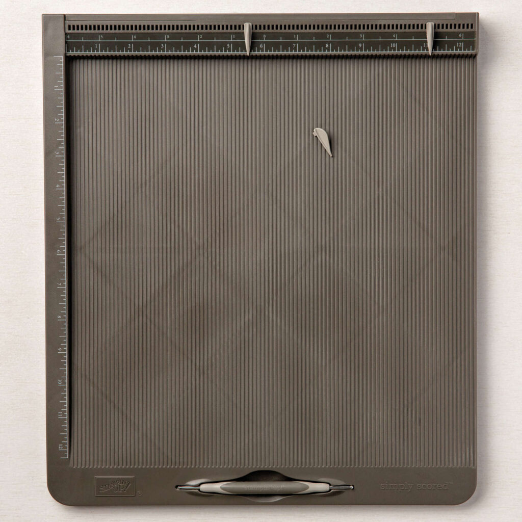 A Simply Scored Scoring Tool has a base slightly larger than 12" x 12" (30.5 x 30.5 cm). The base plate has grooves etched every 1/8" (3.2 mm) and includes rulers on the top and one side; one standard left-to-right ruler and one zero-center ruler, marked in 1/8" (3.2 mm) increments. The board also Includes three place markers and one stylus.