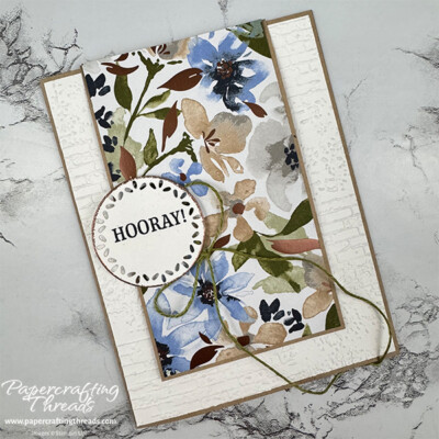 Front of a Hinged Fun Fold Card showcasing the Embossing Powder Technique Borderline. A thin edging of copper embossing powder surrounds a die cut circle with a greeting. Hints of coper foil leaves highlight a floral patterned paper with blues, greens and tans.