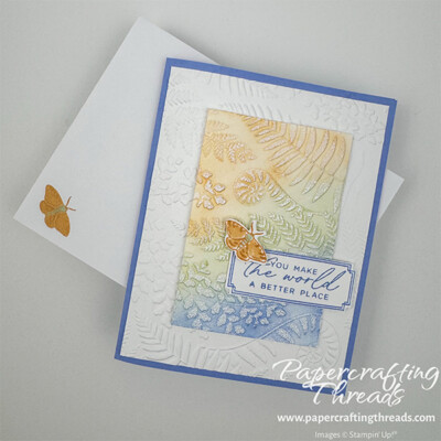 Embossed Spotlight Technique Card features a card base in Hydrangea Hue, a pretty bluish color with just a hint of purple. Ferns and flora are dry embossed into a layer of white cardstock. A large rectangular focal point is dry embossed and colored in swaths of Golden Glow, Soft Sea Foam and Hydrangea Hue colors, with the edges blending into each other. A Golden Glow moth alights on the greeting 'you make the world a better place'. A matching white envelope with a moth on the lower left corner completes the