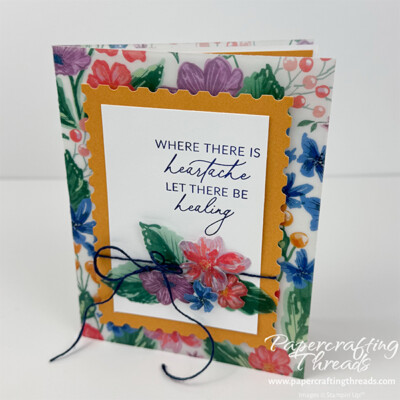 Double Vellum Techniques card with Berry Botanical cardstock vellum folded around white cardstock card base. Watercolor floral and leaf images in purples, blues, pinky reds and greens. Golden Glow two tone postage die cut mat layer behind white focal point with dark blue sentiment in upper right corner. Sentiment is 'where there is heartache let there be healing'. Popped up fussy cut floral and leaf images arranged in a bouquet covers the bottom half along with a dark blue baker's twine thread.