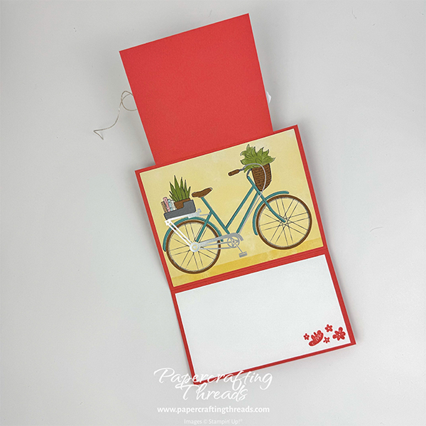 Easy Little Fun Fold card alternative for Bikes & Blooms Paper Pumpkin kit. Card is shown open. Coral colored card base extends above center focal point of a bicycle with plants and books in the baskets. White liner lower panel has stamped flowers in the lower right corner.