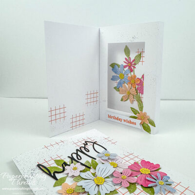 Hidden Shadowbox Fun Fold card alternative for July 2026 Hooray for Birthdays Paper Pumpkin Kit. Front and inside views of a white card base with watercolored floral die cuts in peach, soft pink, soft blues and soft purples. Front has large black greeting of 'happy' along with large spray of florals and greenery with a cross hatch of orange in the background and black splatters of ink. Inner left of card has shadowbox with large floral spray showcased inside the 'box', sentiment of 'birthday wishes' along the bottom and another peachy blossom and greenery. Inner right has more of the orange crosshatch pattern and black splatters.