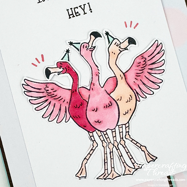 Close up of coloring three flamingo buddies in various shades of pink. Birds have light blue party hats on and partial greeting of "HEY!" shown.