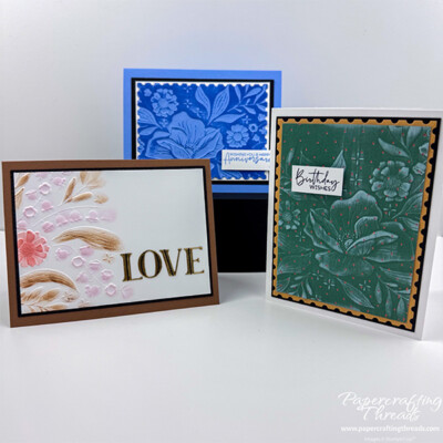 Three techniques with embossing folders, featuring the Floral Spray 3D Embossing Folder, a gorgeous large floral element with graceful leaves and tiny bell shaped flowers. Card on the right has green embossed floral design with copper dots and white ink on the embossed raised portions. Matted on gold, then black and mounted on a white card base. Sentiment is 'Birthday wishes'. Card on the left has portion of the embossed floral images on white background and colored with dark tan, peach and pale pink with large Luxe gold foiled letters spelling out L-O-V-E. Matted on black layer and mounted on dark tan card base. Card in back has large floral image debossed with blue ink on the raised background. White mat on top of black mat and all mounted on blue card base. Sentiment is 'wishing you a happy anniversary'.