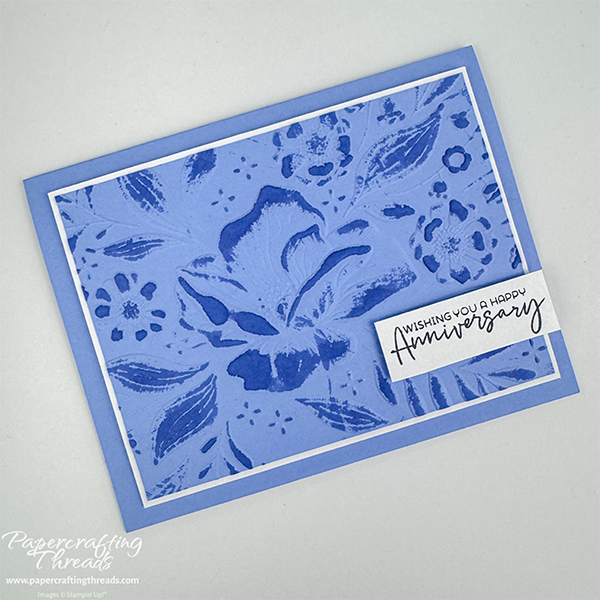 Embossing Folder Technique sample with Floral Spray design raised and ink pad dragged across a few times. Shades of blue and white mat on blue background.