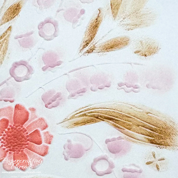 Close up of sponge dauber technique for coloring in an embossing folder design. Floral images colored in dark peach and pale pink with leaves in brown.