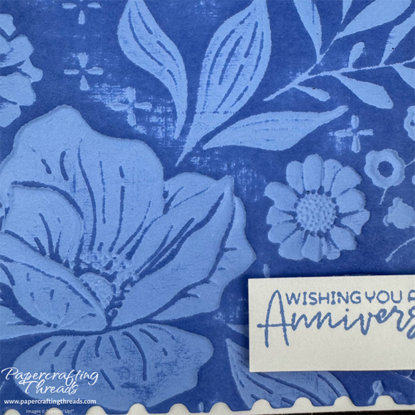 Close up of an embossing folder technique with a large floral image debossed with blue ink on a raised background. Sentiment is 'wishing you a happy anniversary'.
