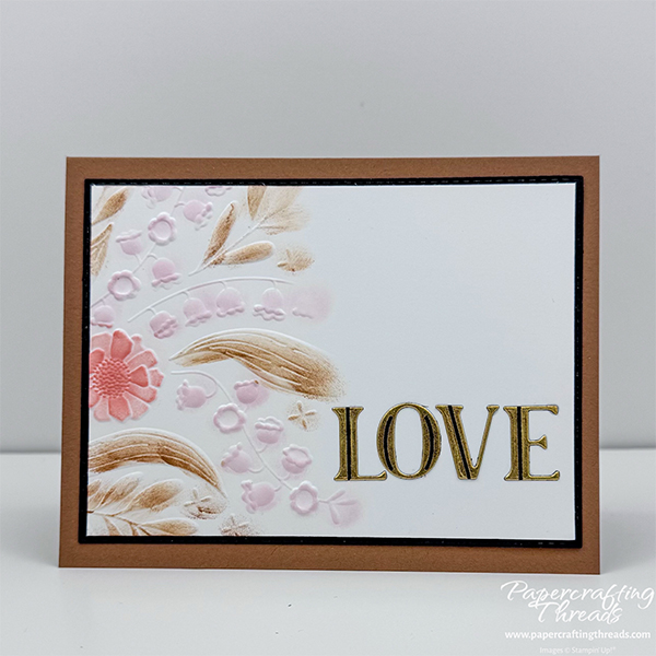 Card featuring an embossing folder technique has portion of the embossed floral images on white background and colored with dark tan, peach and pale pink with large Luxe gold foiled letters spelling out L-O-V-E. Matted on black layer and mounted on dark tan card base.