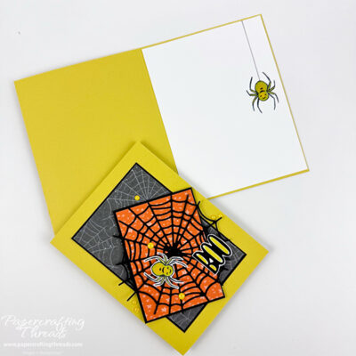 Card Sketch 101 Spider BOO shows front and inside of spider themed greeting card. Card base is acid yellow. Card front has a large black spider web over orange star-patterned paper and over web-patterned paper. A friendly acid-colored spider is in the web. Several acid yellow sparkle dots are scattered in the web. Greeting is a large black BOO with acid yellow centers in the letter openings. Inside of card has an acid yellow spider dropping down from the top on a single web strand.