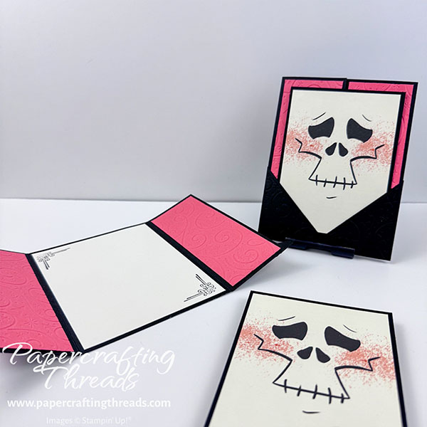 Pocket Gatefold Card shows one card closed, and one open. Black card base with embossed Calypso Coral panels open up to reveal liner with abstract stamped images in corner. Front of card features an oversized skeleton face panel, that pulls free from the triangle corner pockets to allow the gatefold to open.