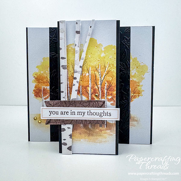 Triple Panel Standing Card Opened Front View. Two narrow panels flank a wider central panel with a scene of golden-leaved aspen trees on a black card base. A speckled trunk overlays the grove. Two leaf-embossed narrow strips flank the center panel. A brown wood-like label sets off the sentiment strip that reads 'you are in my thoughts'.